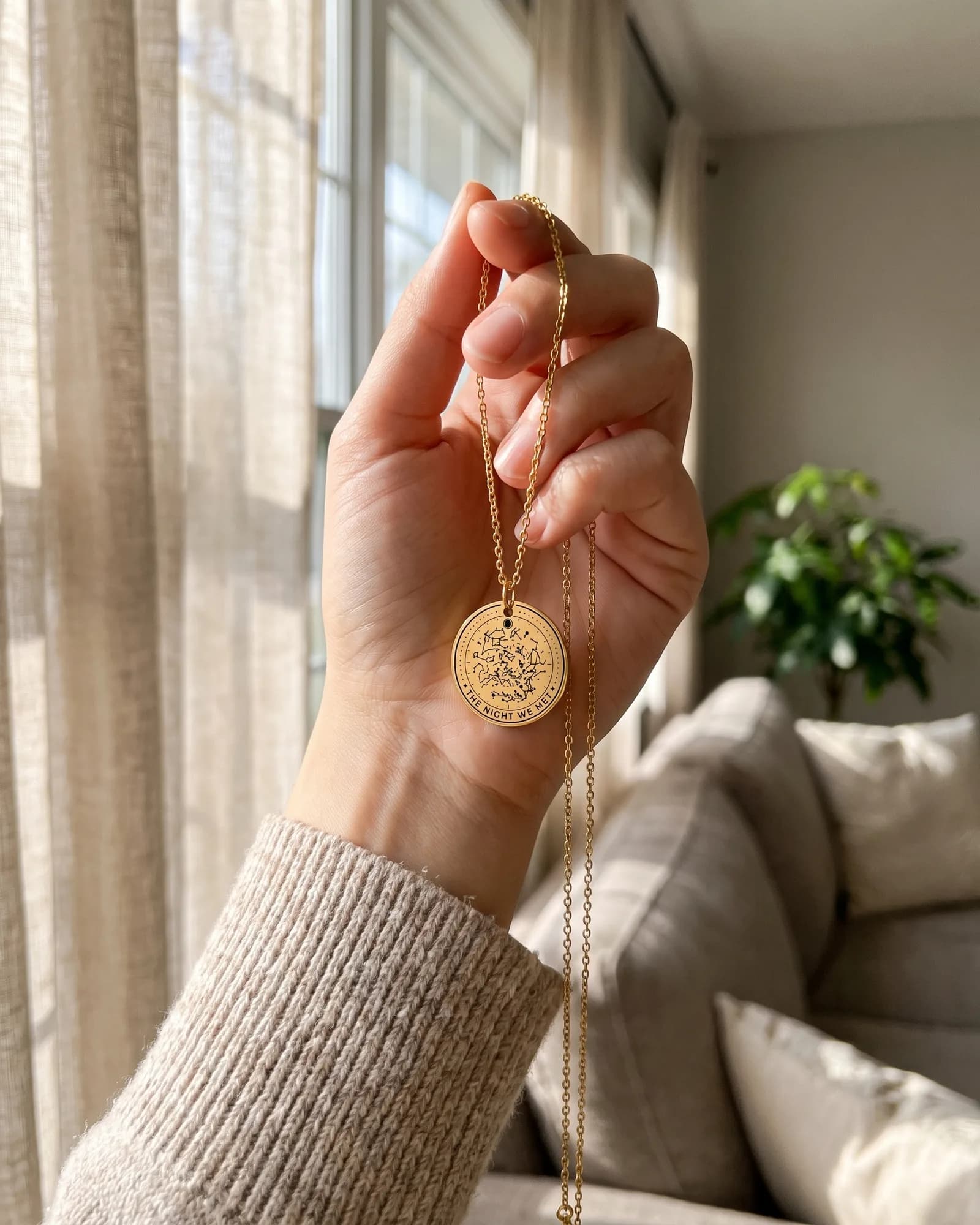 A gold plated star map coin necklace held up by its chain in window light, The Night We Met around the rim
