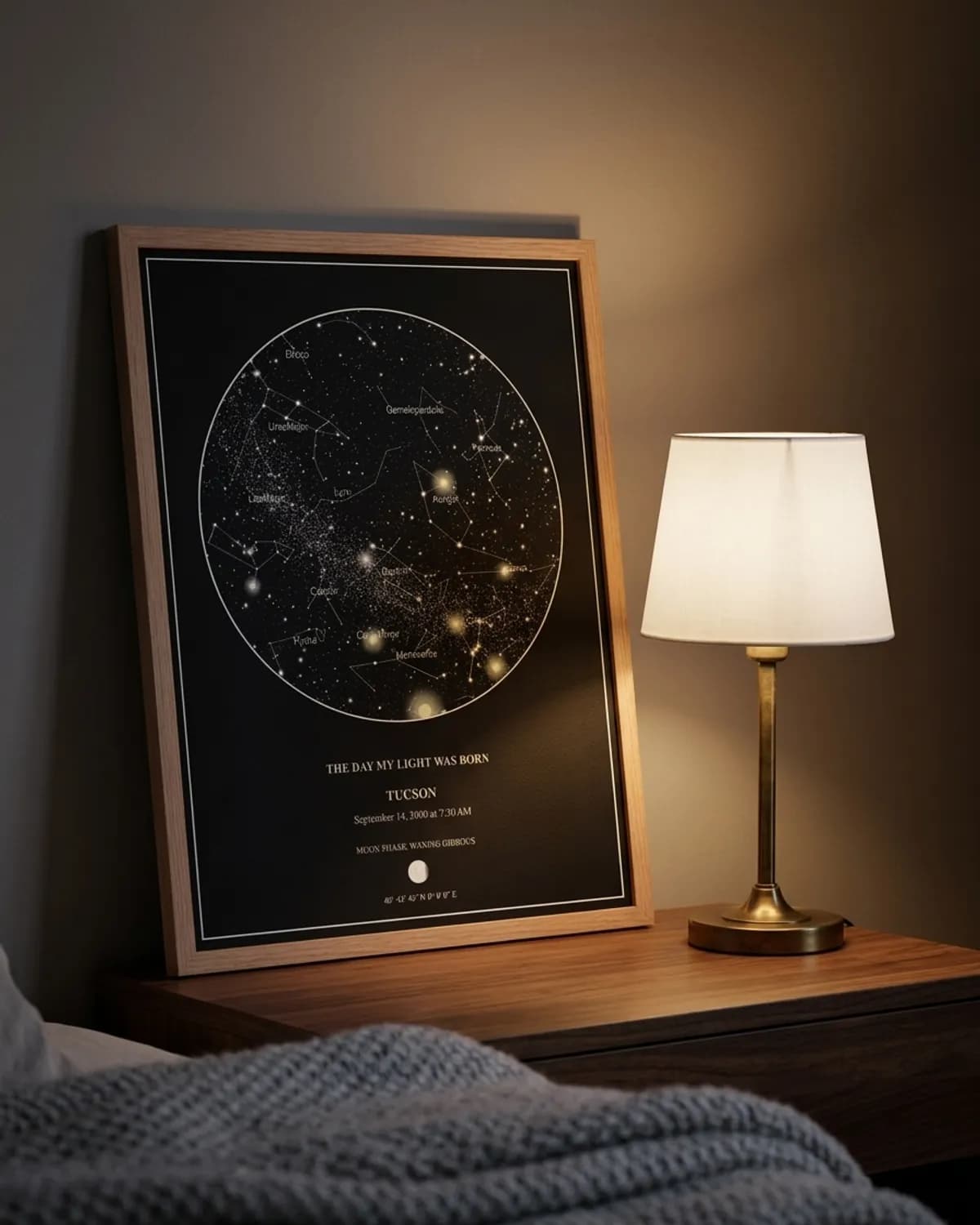 Oak-framed star map print on a bedside table beside a brass lamp