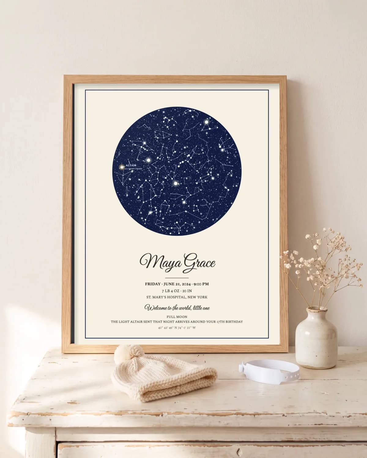 Framed birth poster with the night sky on a nursery dresser beside a knitted baby hat and hospital bracelet