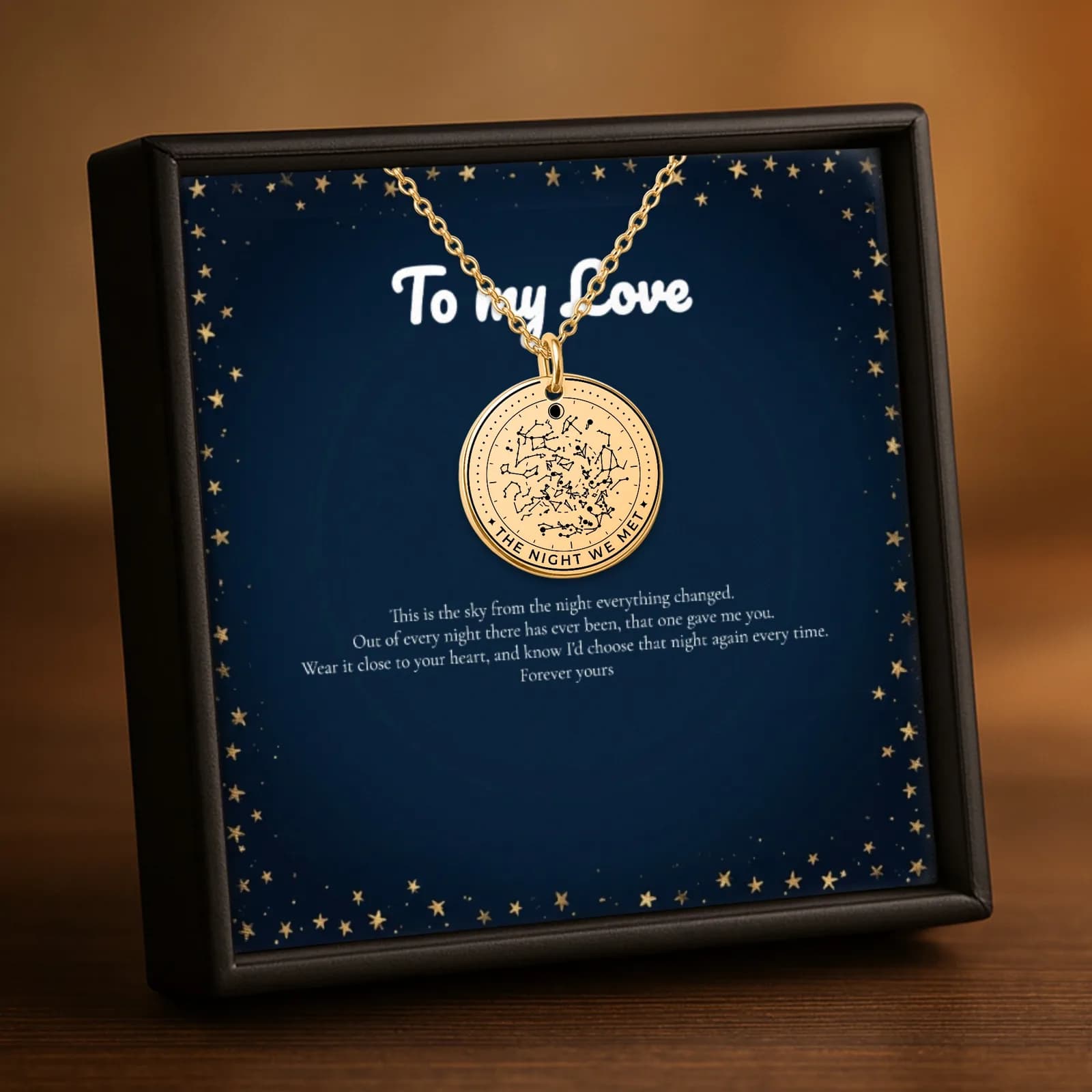 A gold star map necklace in its black gift box, hanging over a navy message card that reads To my Love