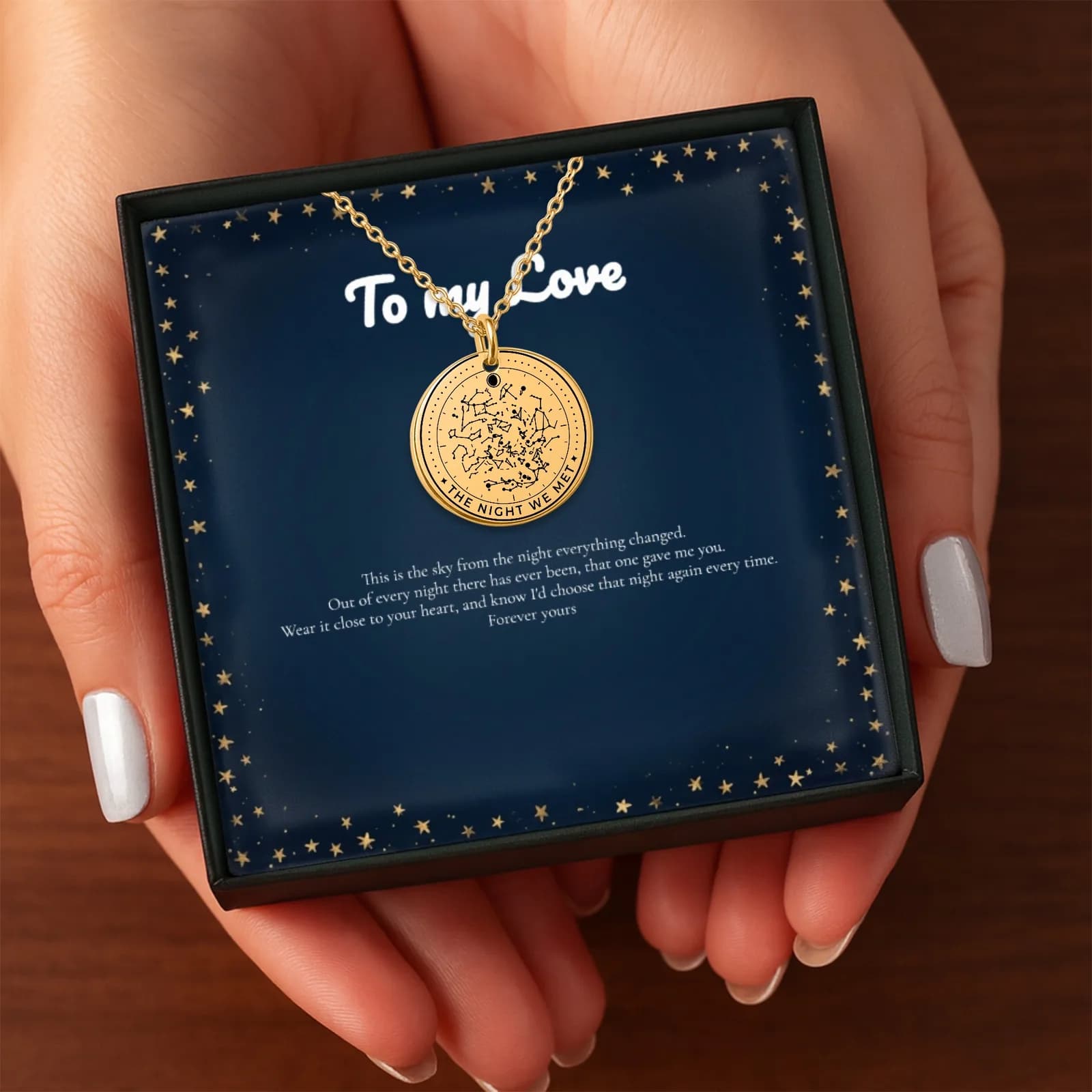 Two hands holding out the gift box with a gold star map necklace inside