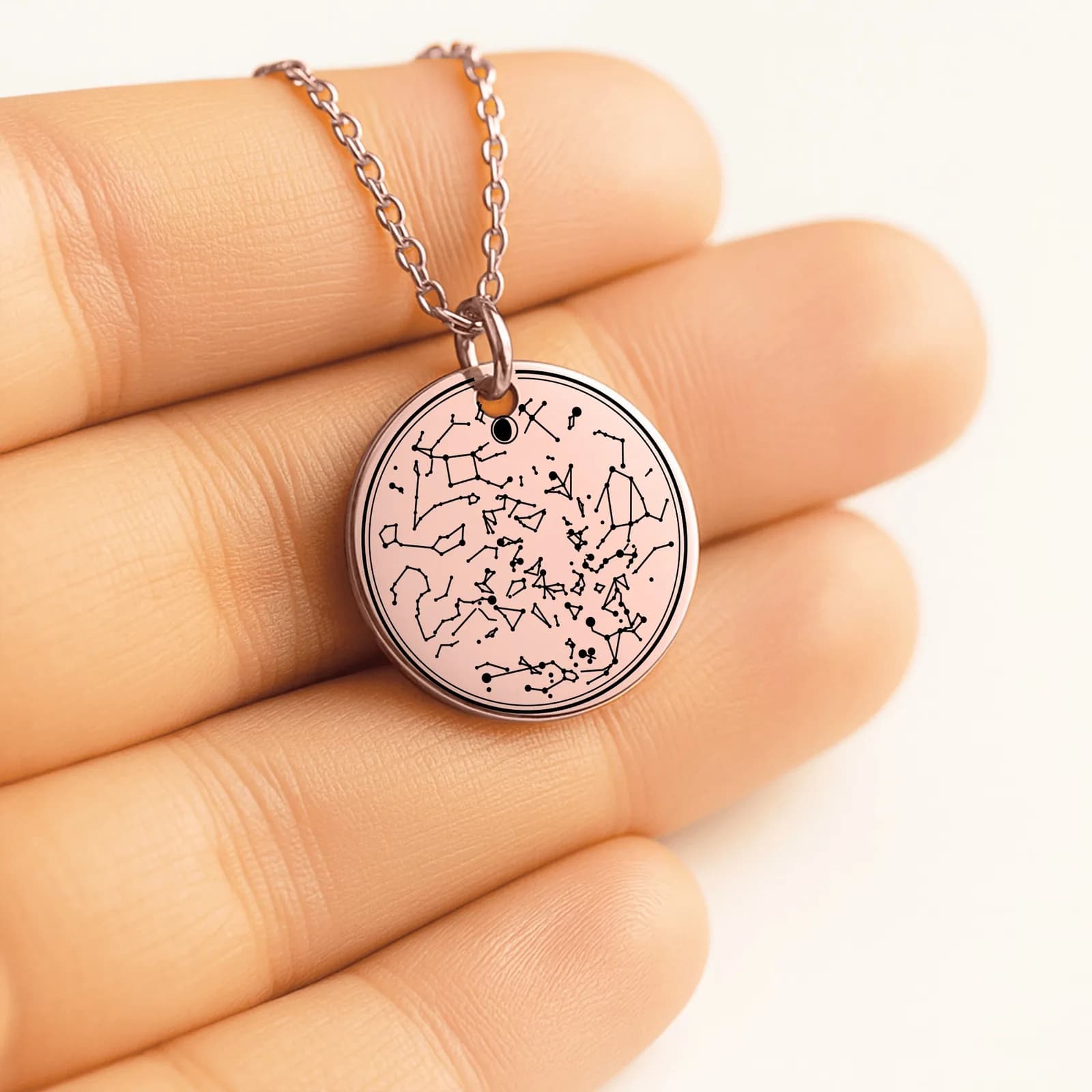 A rose gold star map coin resting in an open palm, engraved with the constellations of one night