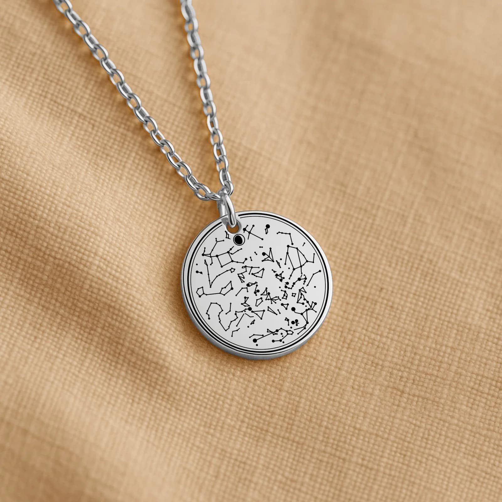 A silver-tone steel star map necklace lying flat on beige linen