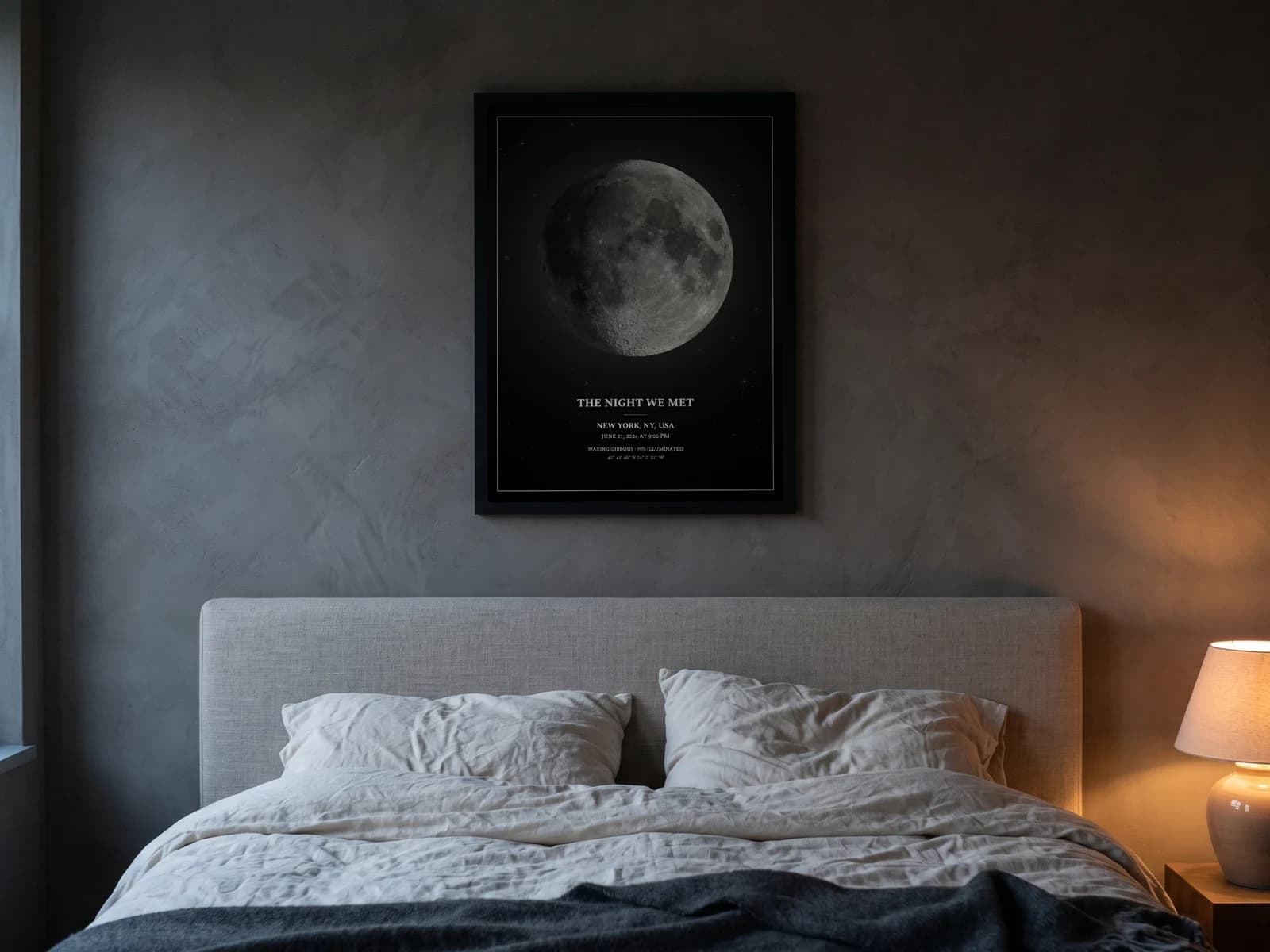 Moon Phase Poster in Pure Noir, black-framed above a bed with linen bedding